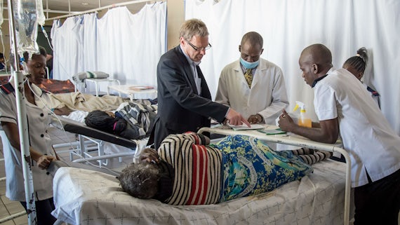 Dr Andrew Freedman talking to hospital staff in Northern Namibia, next to a hospital bed where a patient is lying.