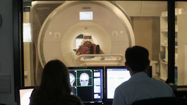 A participant lies in an MRI scanner while a male and female researcher operate the scanner