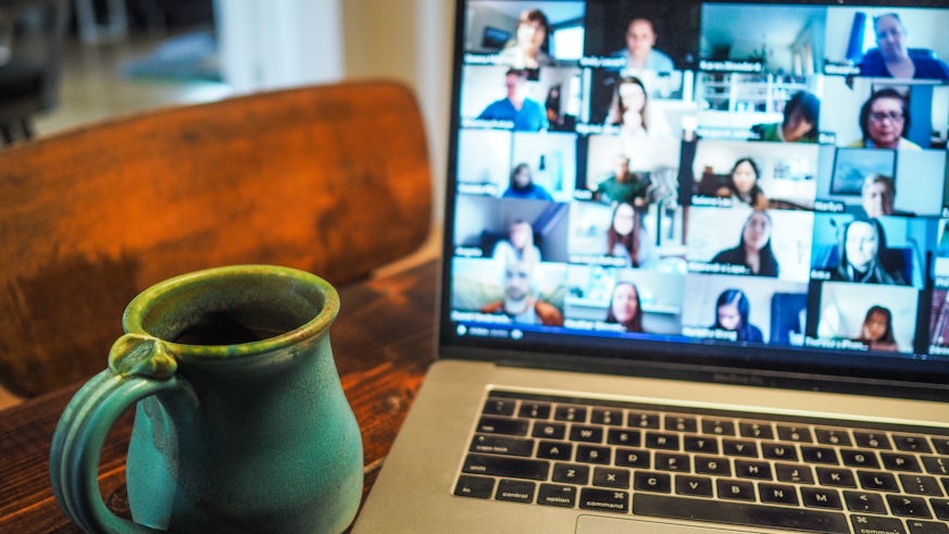 A laptop showing a zoom call with lots of people and a cup of tea on a table