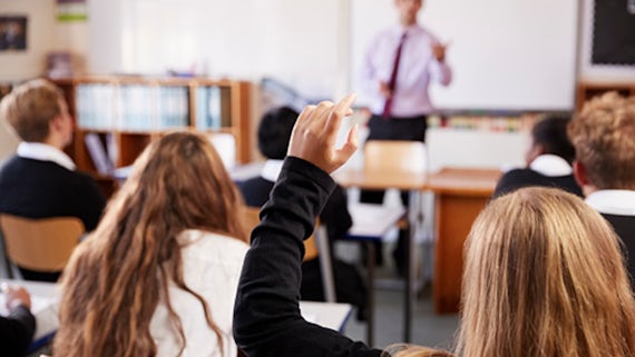 Pupil in focus with hand raised in classroom