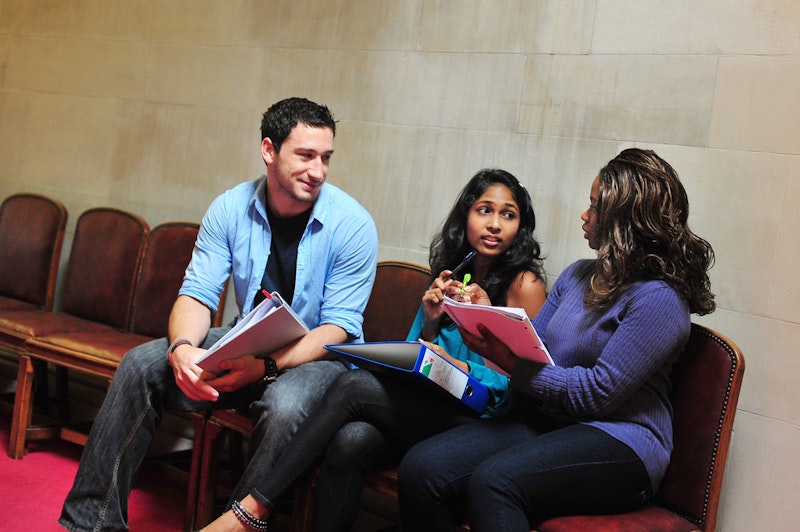 Three people sat on seats in a hallway