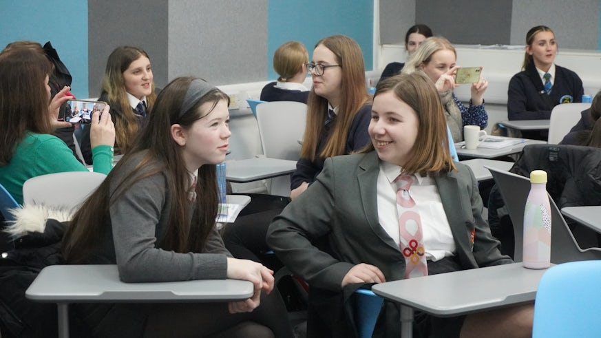 A room of female pupils looking at each other and smiling.