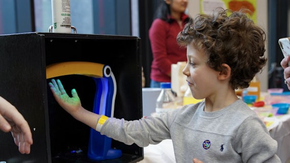 A young boy looks at his hand under ultraviolet light.