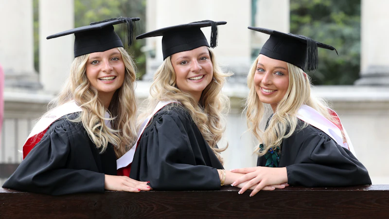 Three female graduates sat on a bench in their hats and gowns.