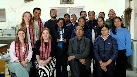 A group of women and men pose for a photograph in a lab at the Nepal Academy of Science and Technology