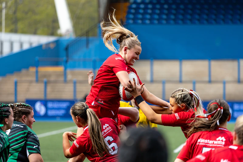 A female rugby player wearing a red jersey holds a white ball after catching it at a lineout.