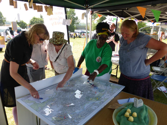 Five people gather around a table, looking downwards toward a map.
