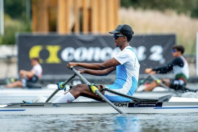 A side view shot of a sportsman rowing in a race taking place on a river. Two other rowers are in the background. 