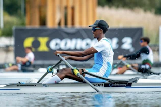 A side view shot of a sportsman rowing in a race taking place on a river. Two other rowers are in the background. 
