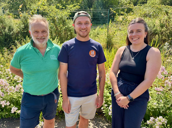 Three people smiling directly at the camera lens on a sunny day. 