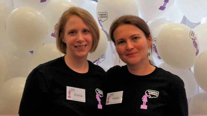 Two female participants of the event smiling in front of balloons.