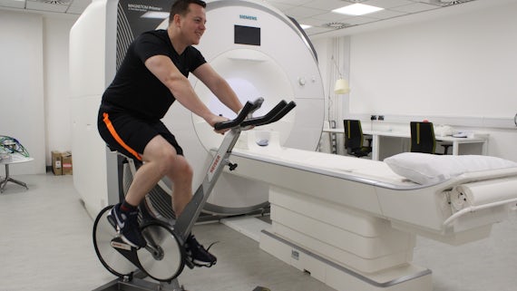 Photograph of a man on an exercise bike in front of an MRI scanner