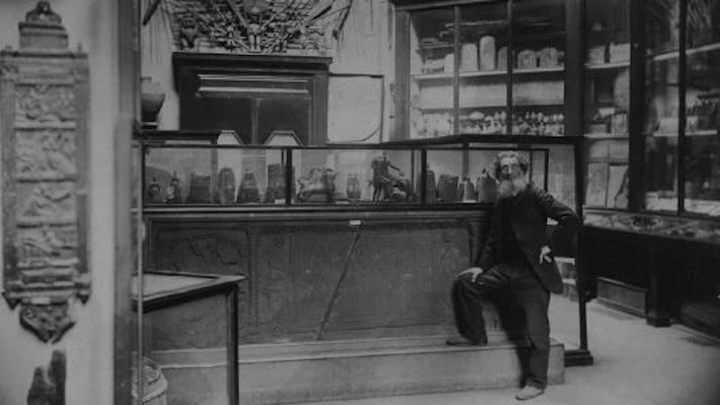 A black and white photograph of Joseph Anderson standing among the archaeology displays in the Royal Institution in Edinburgh. 