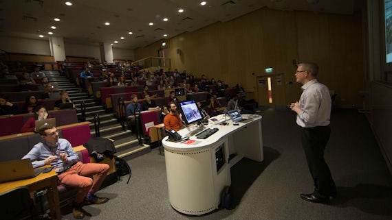 An audience of neuroscience researchers sit in a lecture theatre while a speaker gives a talk at the front of the room