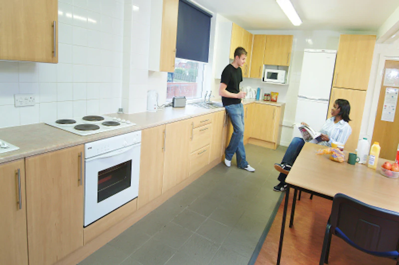 Kitchen area with two people talking, one seated, the other leaning against cabinet.