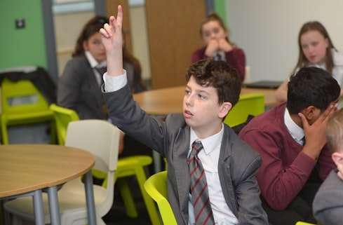 A boy puts his hand up in a classroom to answer a question. 