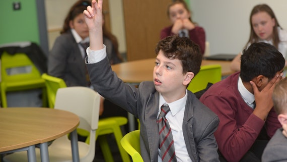 A boy puts his hand up in a classroom to answer a question. 