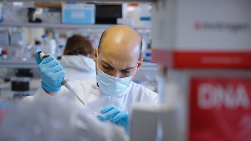 researcher working in lab wearing a mask and holding a pipette