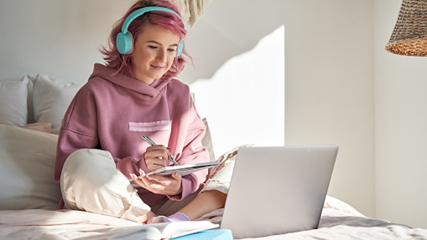 A young person with pink hair works at laptop