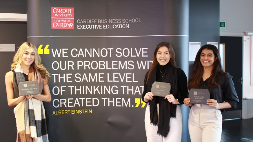 Three awards winners stand in front of a sign in Cardiff Business School