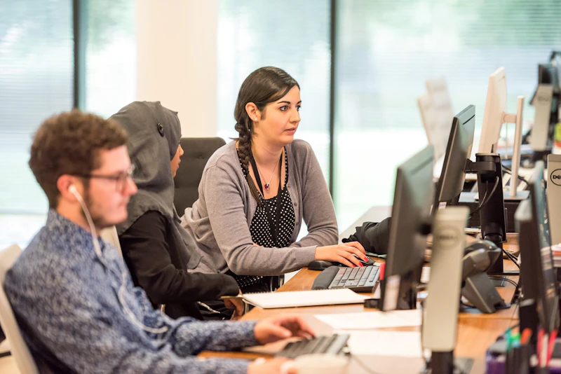 three people sit at desks with headsets in a call centre office