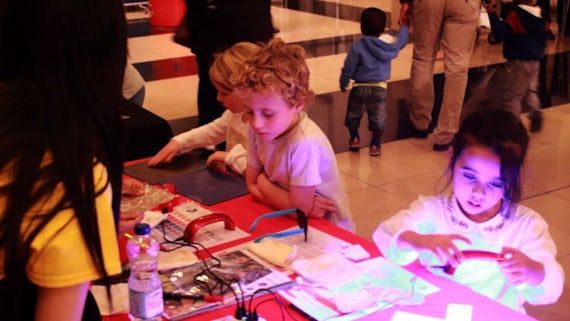 Three children are stood in front of a table in the foyer space of a museum. On the table are various interactive activities