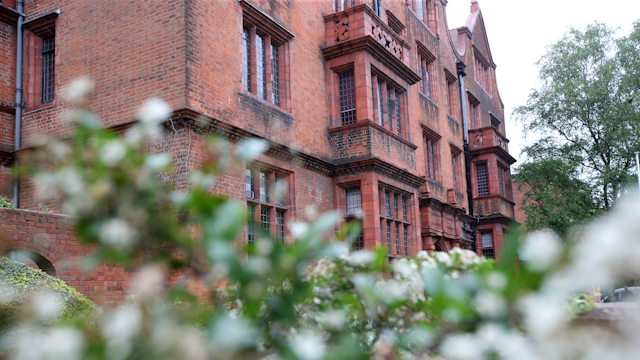The red brick front of Aberdare Hall viewed from behind some blossoming plants. The plants are in soft focus.