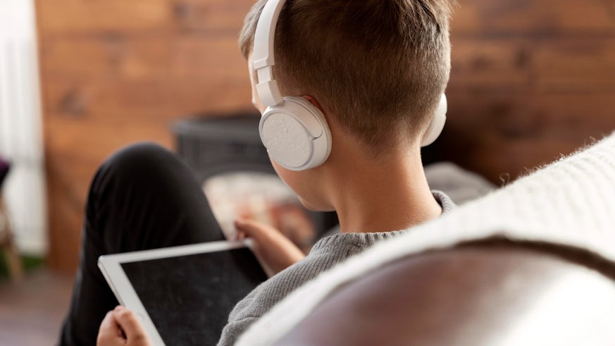Young male child with back to photographer looking at tablet, wearing headphones