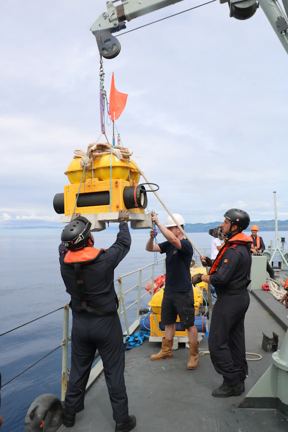 A photograph of researchers lowering a piece of equipment into the ocean from the deck of a ship.