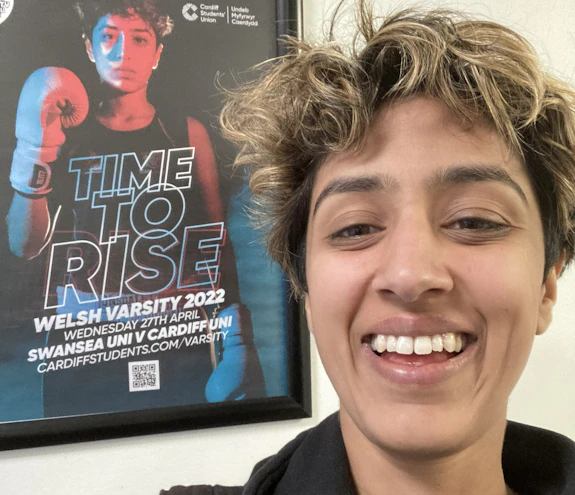 Zara Siddique smiling in front of her boxing match poster