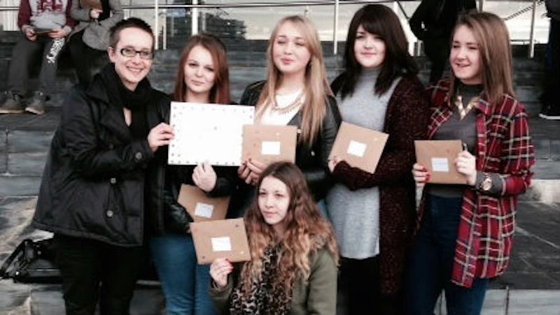 Female students standing outside the Senedd in Cardiff Bay, holding Valentine cards for an anti-abuse campaign
