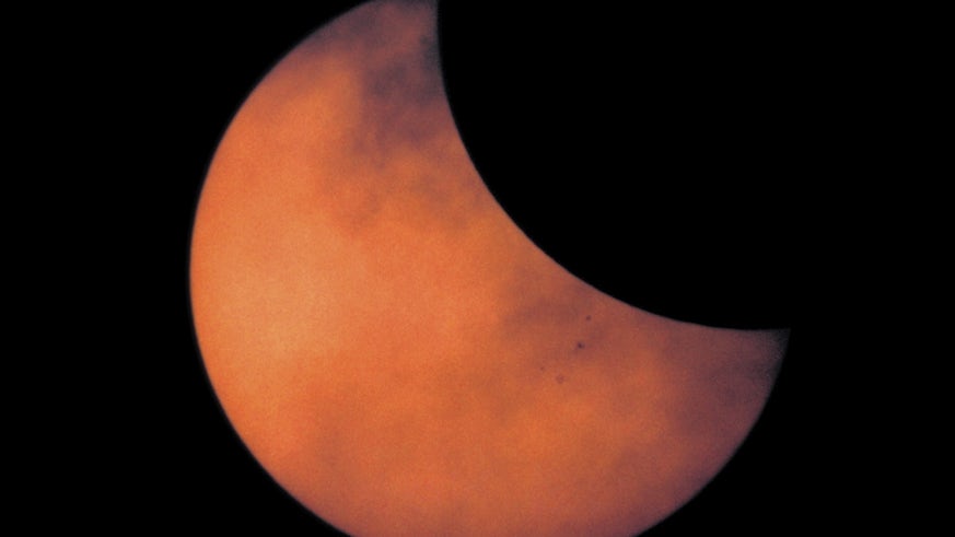 Sky with bright orange sun partly covered by moon