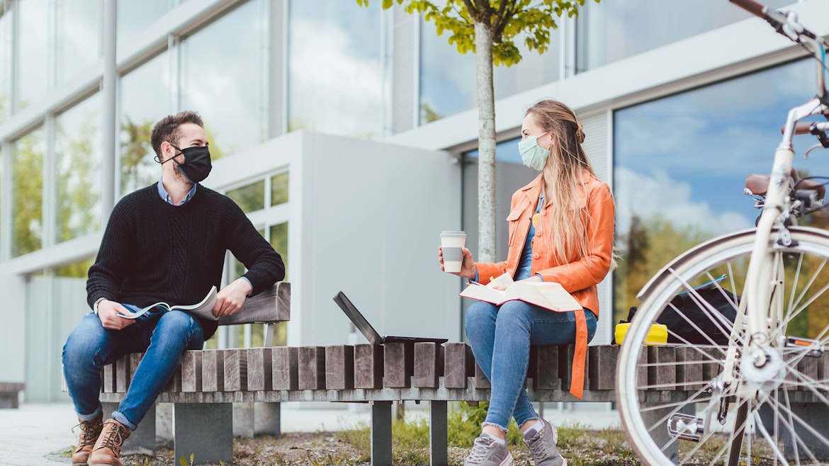 Two masked students talking on a bench