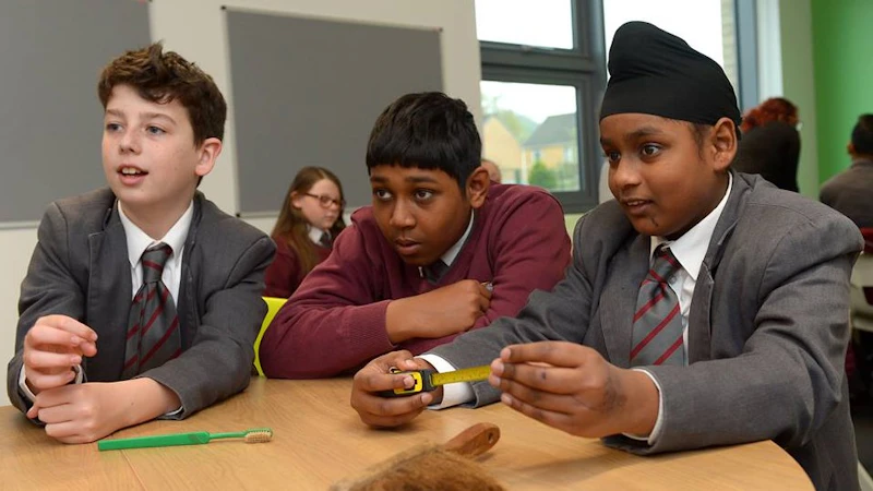 Three young students sat round a table listening.