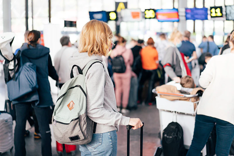 a young person with a packback and case waits in immigration queue