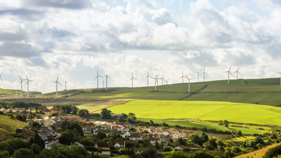 A photo of a Welsh town and hills in the background with wind turbines