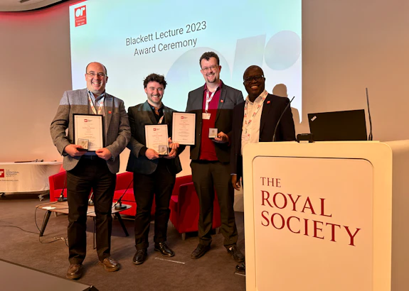 Four researchers are photographed on a stage at The Royal Society. Three are holding certificates and medals.