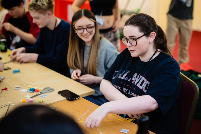 Participants working at a table on a bracelet making craft activity involving coloured threads during the Step Up summer school.