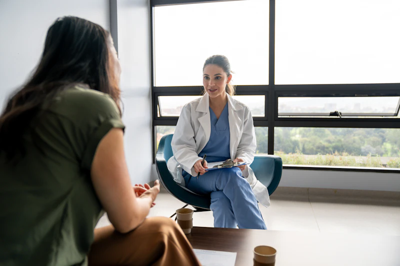 Female doctor talking to a female patient in a consultation at the hospital while taking notes on a clipboard