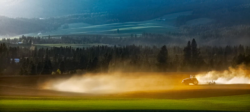 A tractor ploughing a farm field and creating a cloud of dust behind.