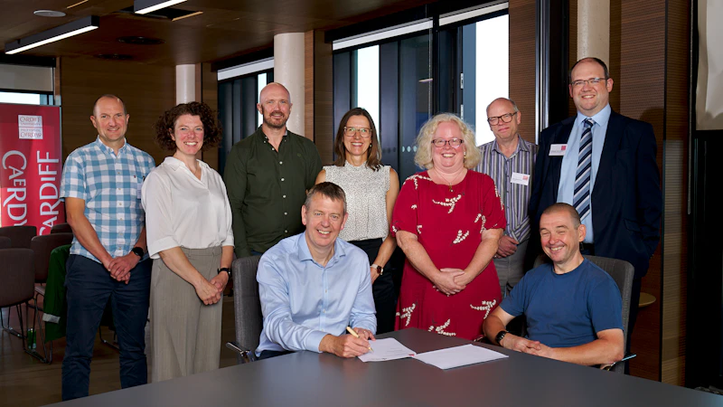 Professor Steve Riley, Cardiff University Pro-Vice Chancellor, College of Biomedical and Life Sciences, and Iain Bell, National Director for Public Health Knowledge and Research, signing the Memorandum of Understanding, surrounded by colleagues