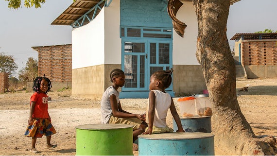 Three children play under a tree, in front of a building on the site of Shiyala School.
