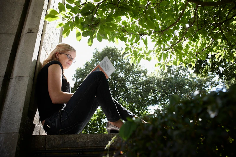 Female student sitting on a wall reading a book