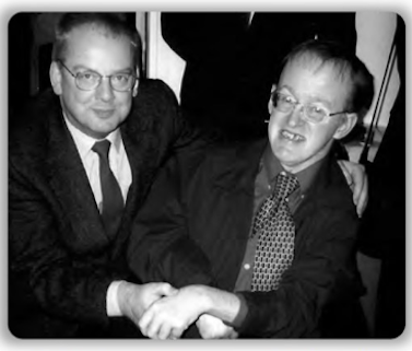 Black and white photo of two men smiling, their hands touching. They are smiling and looking happy. 