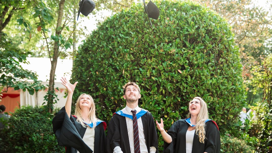 Two female and one male student wearing graduation gowns and throwing their mortar boards in the air
