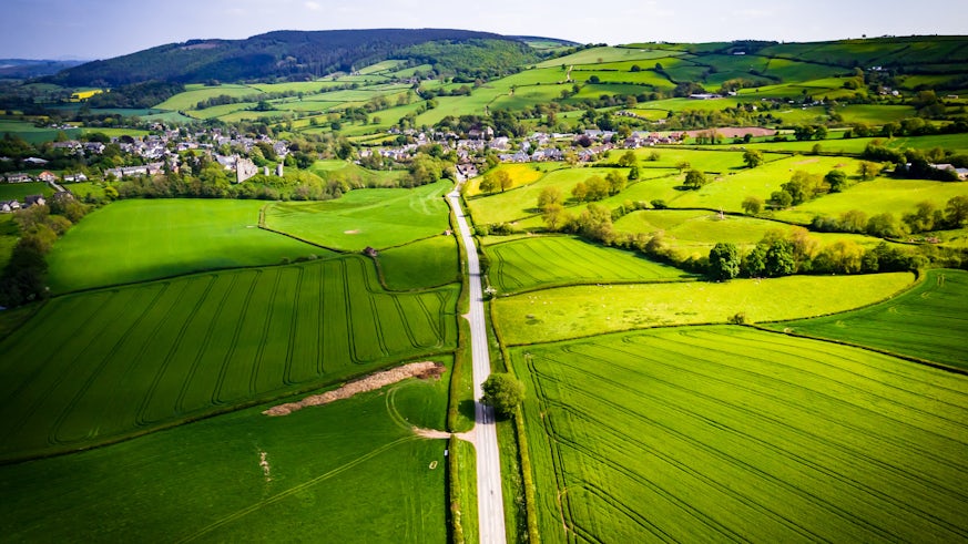 Aerial view looking down on a rural road in the UK countryside with a car racing along it. - stock photo. On a bright sunny day, farmland and crops can be seen either side of the road 