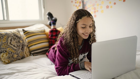 Teen girl using laptop in bed stock photo