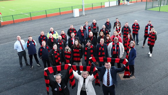 Crowd of delegates holding Cardiff University Sport scarfs above their heads at opening of Llanrumney Sports Fields