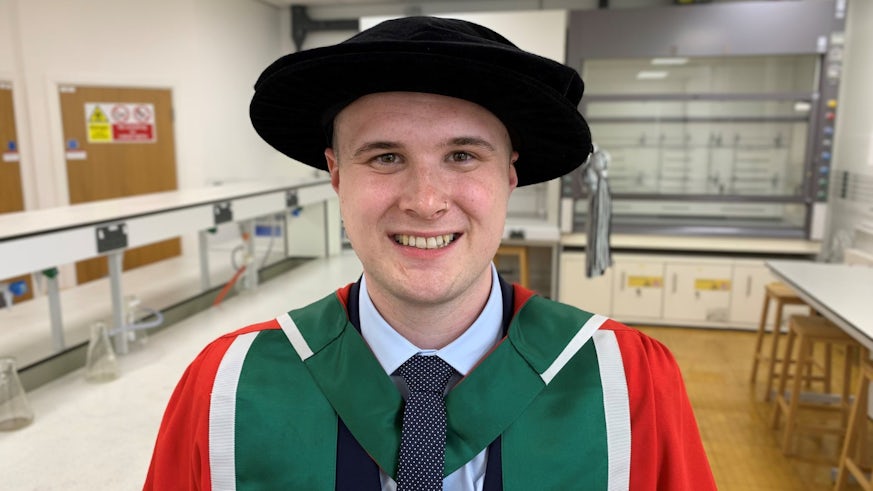 A young man wearing a Cardiff University doctoral gown coloured green, red and white with a black bonnet.