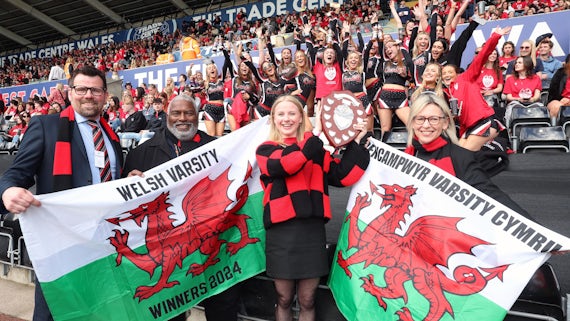 A crowd of people in a stadium facing the camera and celebrating. Cardiff University, winners of the Varsity Shield 2024